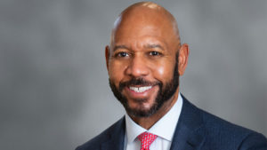 A headshot portrait of Ather Williams III, dressed in navy blue coat, white shirt, and red print tie.