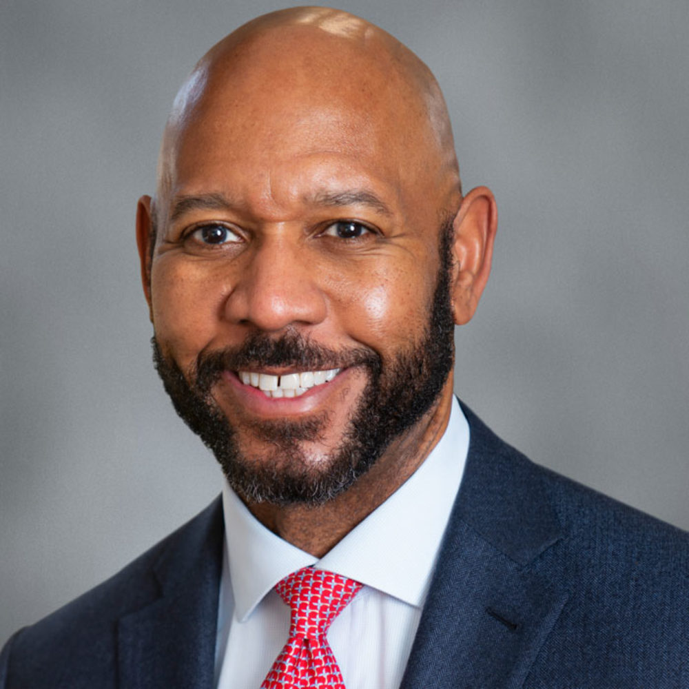 A headshot portrait of Ather Williams III, dressed in navy blue coat, white shirt, and red print tie.