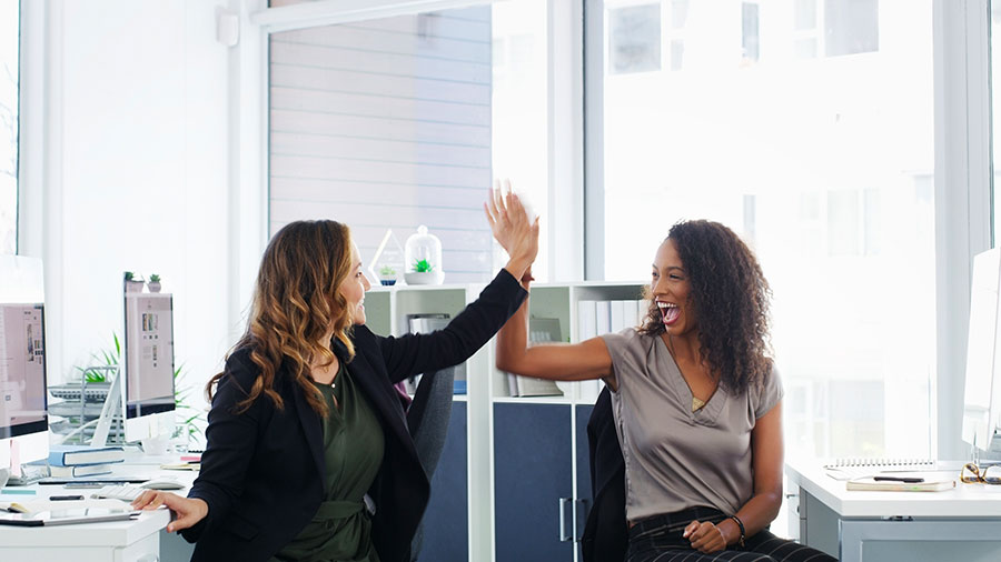 Two women exchange high-fives between their office cubes.