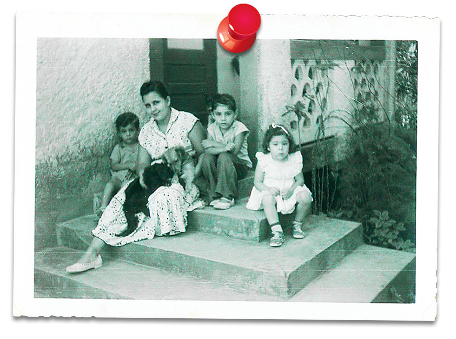 A black and white photo shows Carmen Nazario as a child with her mother and siblings on the porch of their home in Puerto Rico.