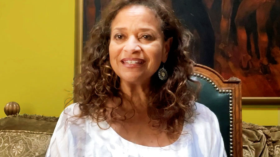 Debbie Allen sentada en una silla sonríe a la cámara. Detrás de ella se ven parcialmente un sofá y un cuadro.