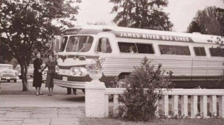 A black and white photo shows two smiling women standing in front of a James River bus