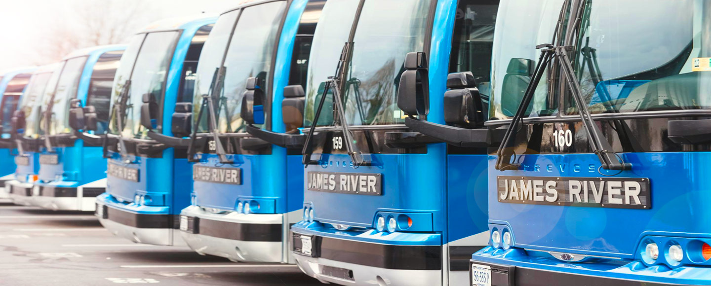 Five blue James River buses are parked side-by-side