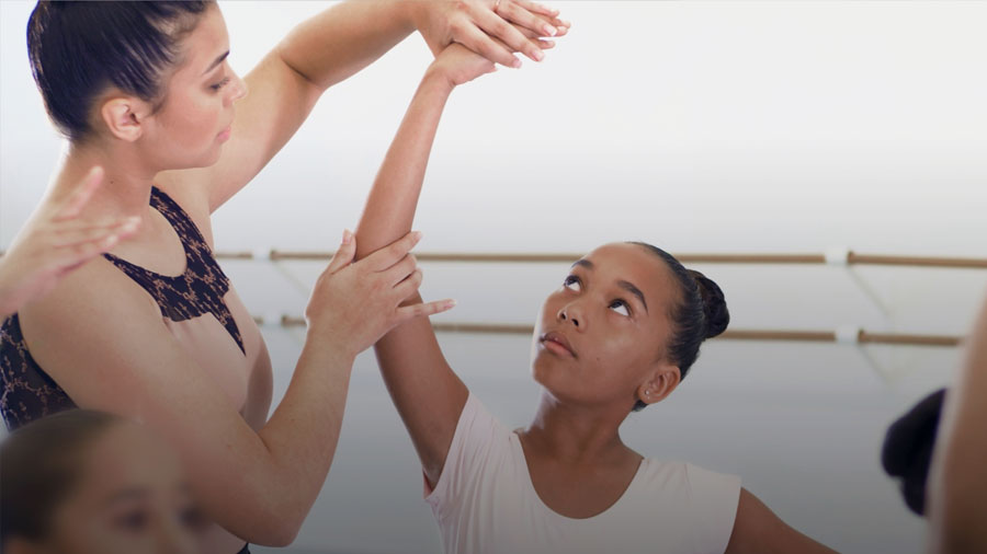 ballet teacher helps a student by holding her arm