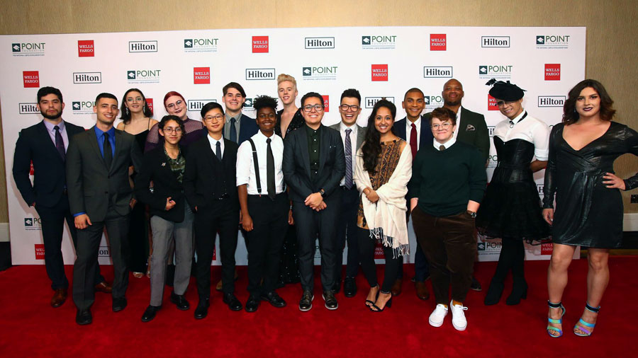A group of students in dressy attire stand on a red carpet in front of a banner with the logos for Point Foundation, Hilton, and Wells Fargo.