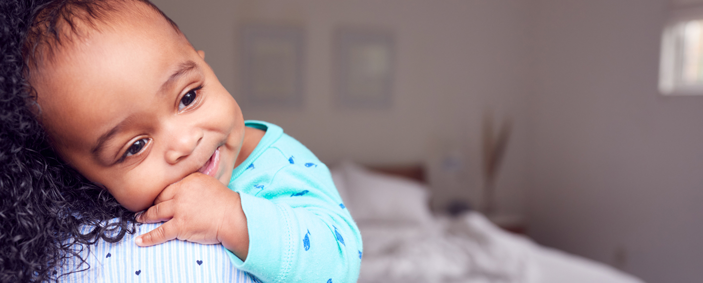 A baby lays on a person with long hair's shoulder.