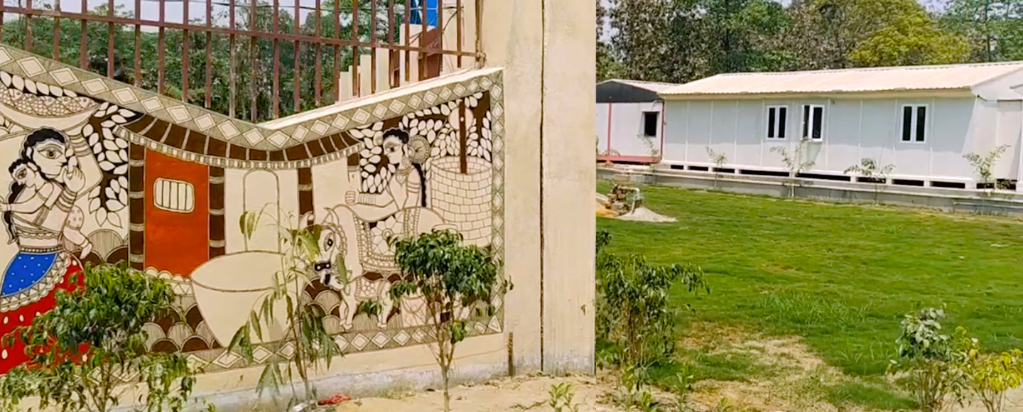 ornate gate with depictions of women and children in foreground, with a modular white building behind it.