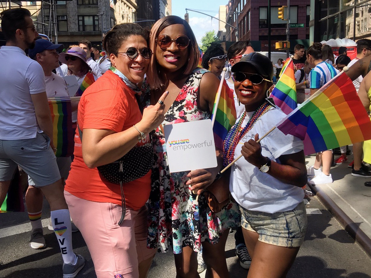  Monique Evans and two friends at a Pride event. The person on the right is holding Pride flags. Evans is holding a sign saying 'you are empowerful.'