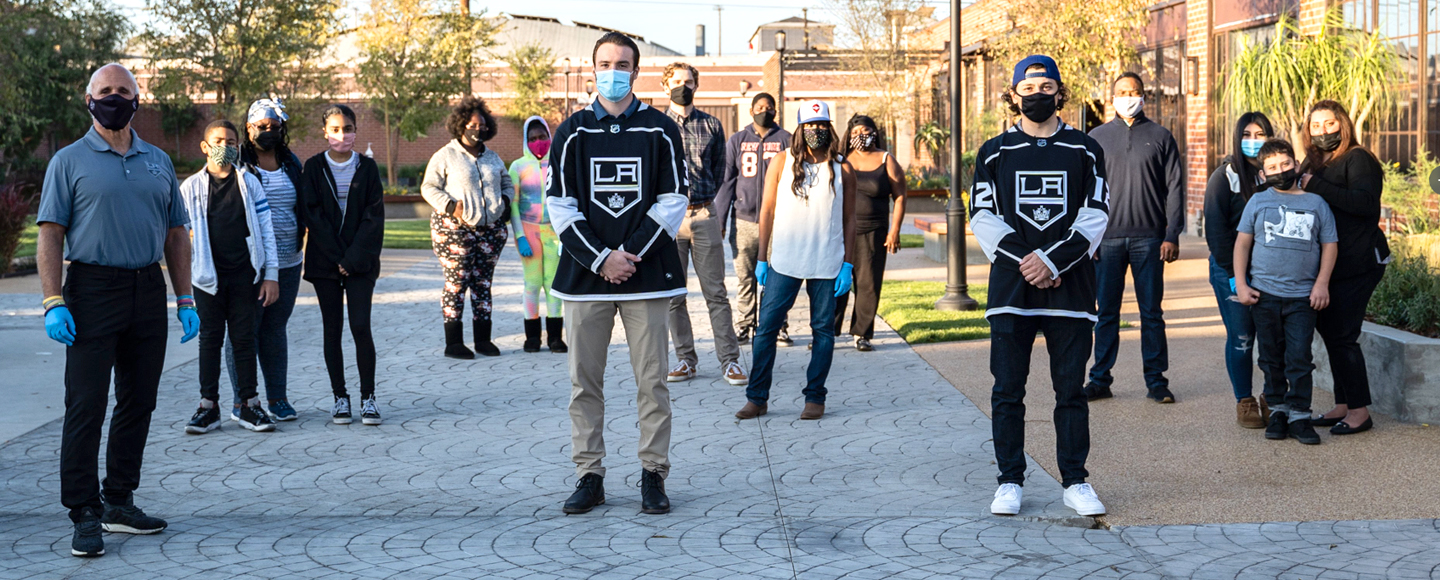 Several groups of people wearing facemasks stand in a semi-circle in a courtyard. Members of the LA Kings stand in the foreground.