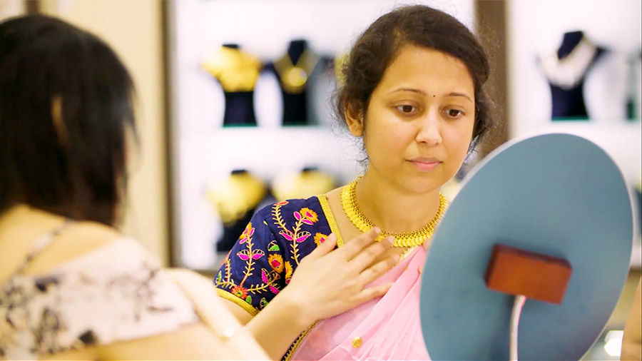 A woman touching a gold necklace around her neck looks into a mirror at a jewelry store.