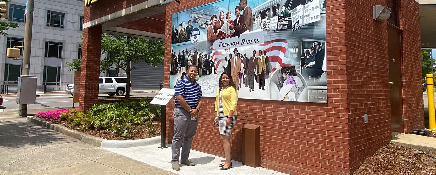 Alex Gay and Monique Henderson stand in front of the Wells Fargo mural honoring the Freedom Riders.