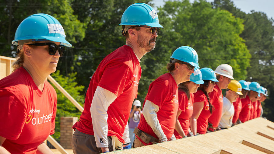 A group of people in hardhats lift the wall of a home under construction.