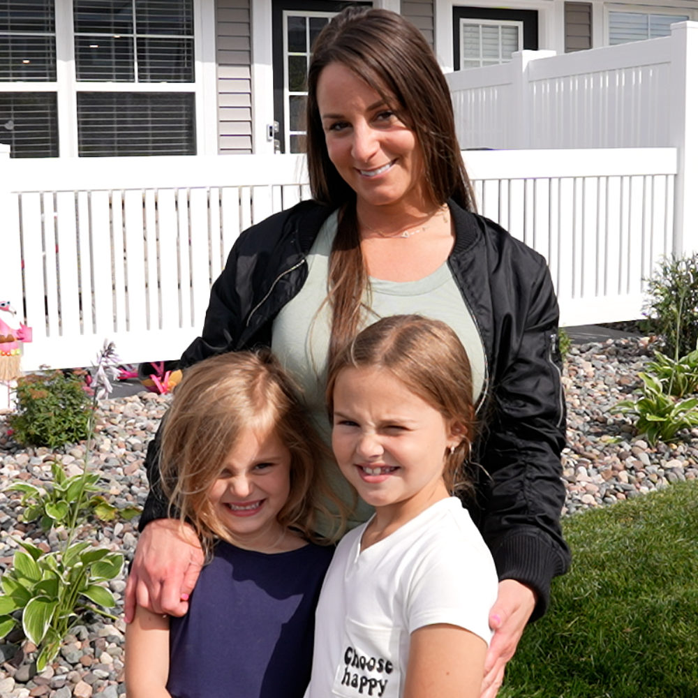 A woman and her two young daughters pose in front of their new home.