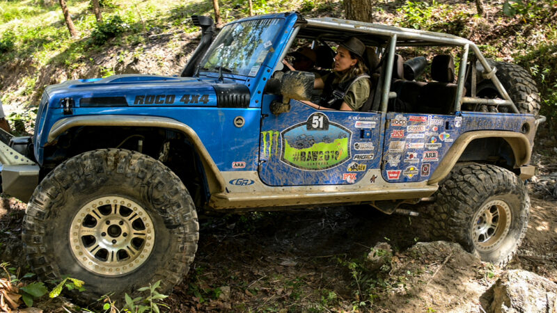 A woman navigates a jeep through rough terrain.