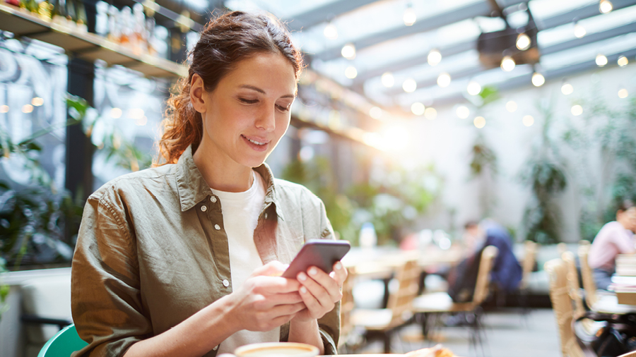 A woman sits in a well-lit restaurant staring at her mobile phone.
