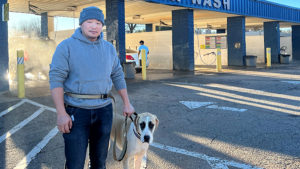 Xiaobo Guan stands holding onto a leashed dog in front of his car wash business.