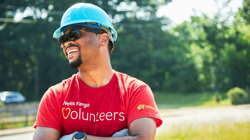 Wesley Brooks, wearing a hard hat and a red Wells Fargo volunteers T-shirt, is smiling outside.