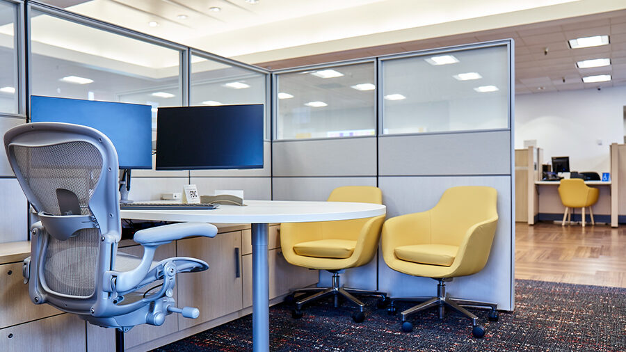 An open office space with bright yellow seating and a desk with large dual monitors.