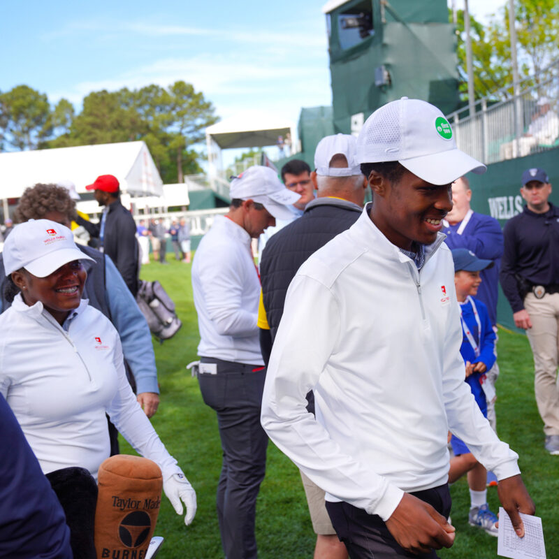 Two golfers smile as they walk off the course with a crowd of people in the background.