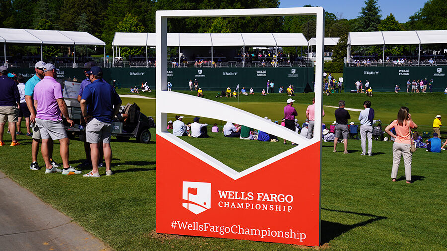 People are scattered about a golf course with a Wells Fargo Championship sign in the foreground.