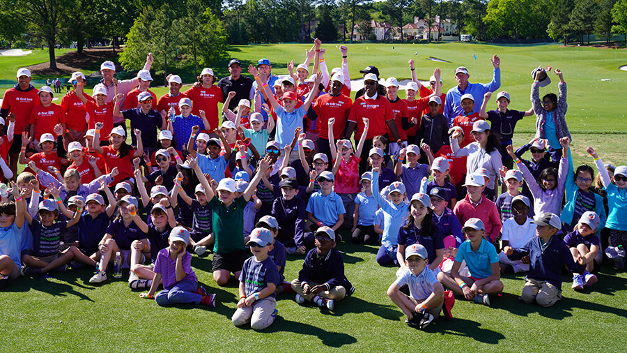 A large group of kids and adults pose on a golf course.