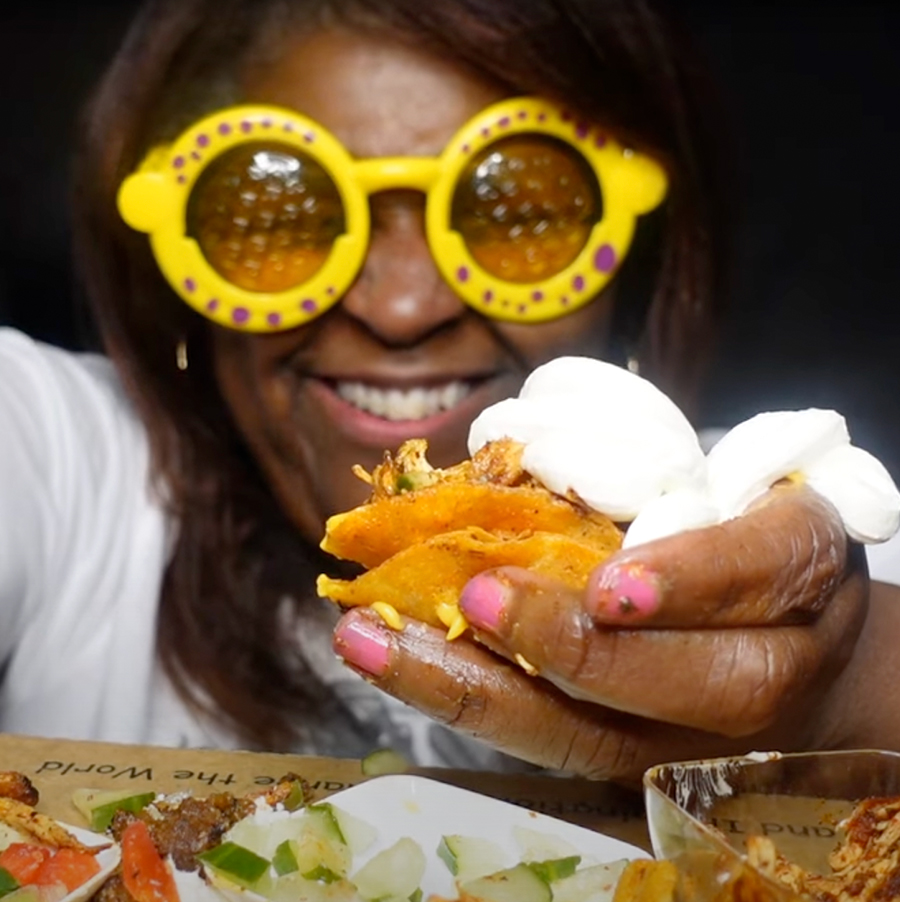 A person wearing yellow rimmed glasses holds a tiny taco.