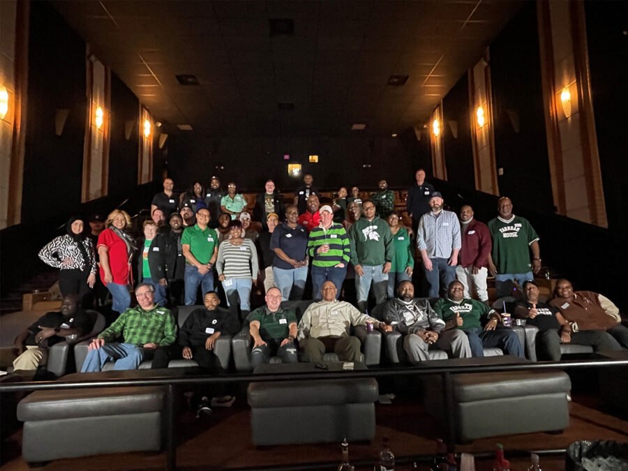 A group of people standing in a movie theater ready to watch the NCAA championship.