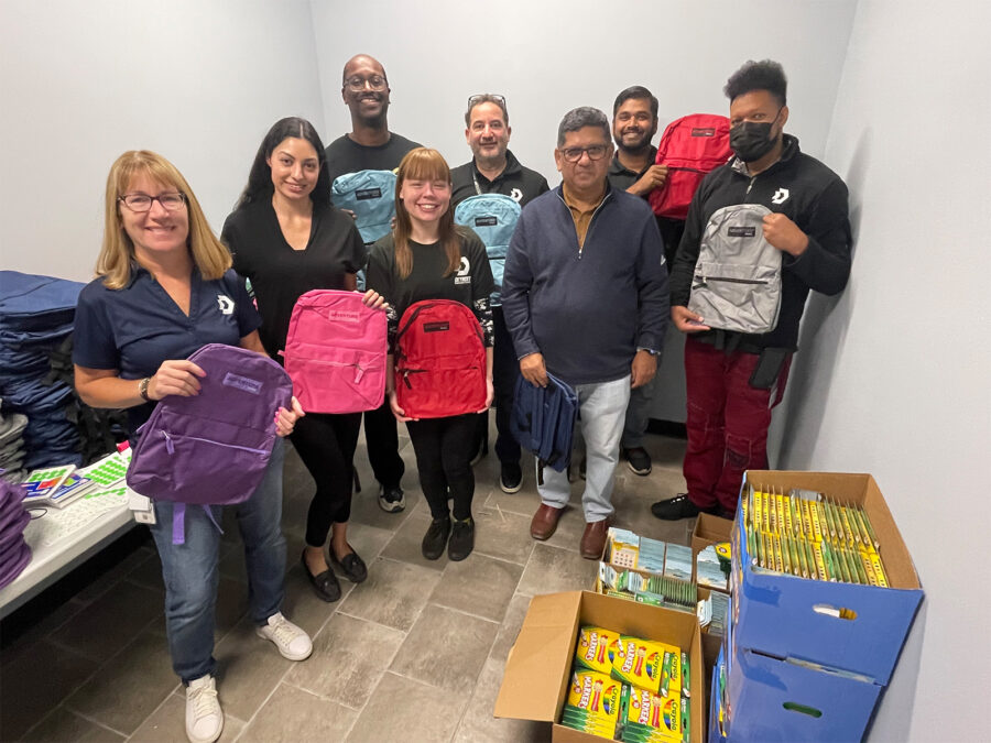 A group of people hold backpacks, ready to be filled with school supplies to be donated to the Children's Center in Detroit.