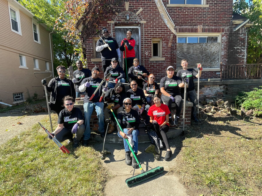 A group of volunteers hold yard tools in front of a home.
