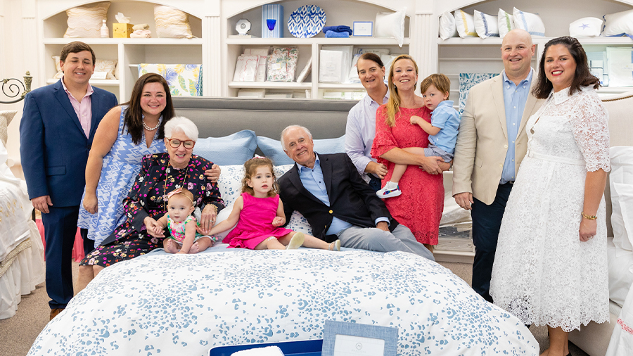 Several generations of people sit and stand around a bed in the Pioneer Linens store.