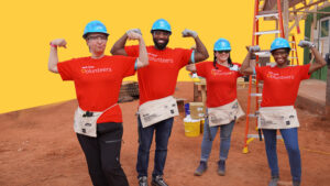 Four people in construction hats and red volunteer shirts pose for a photo