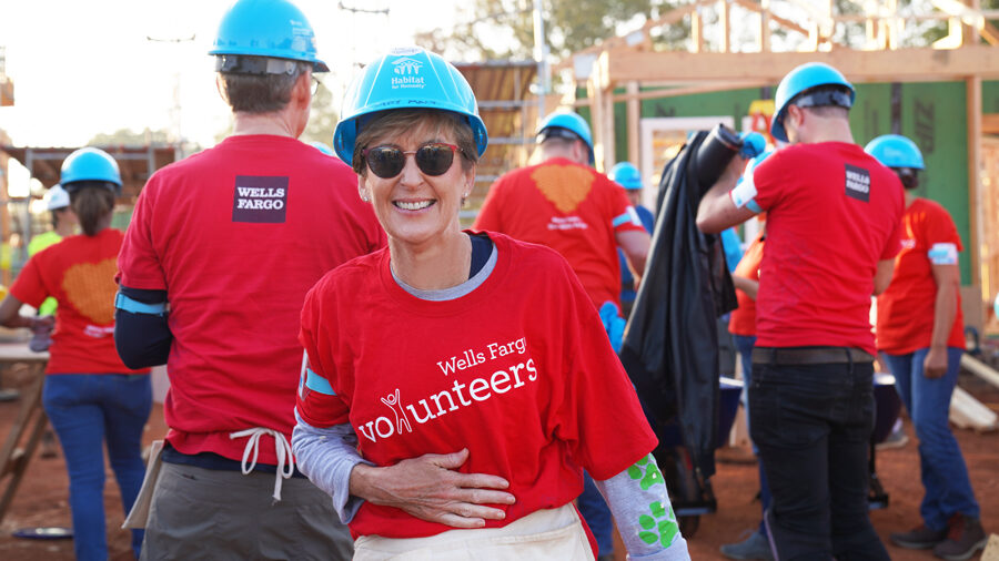 A woman in a red volunteer shirt and blue construction hat smiles for a picture at a construction site.