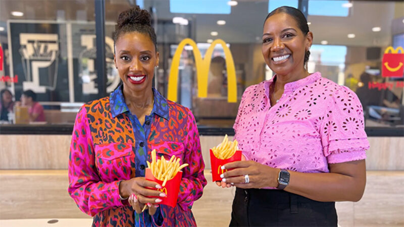 Two women holding boxes of french fries stand inside a McDonald’s restaurant.