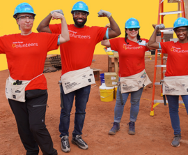 Four people in construction hats and red volunteer shirts pose for a photo.