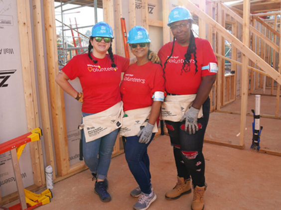 Three women take a break from working and pose in an unfinished home.