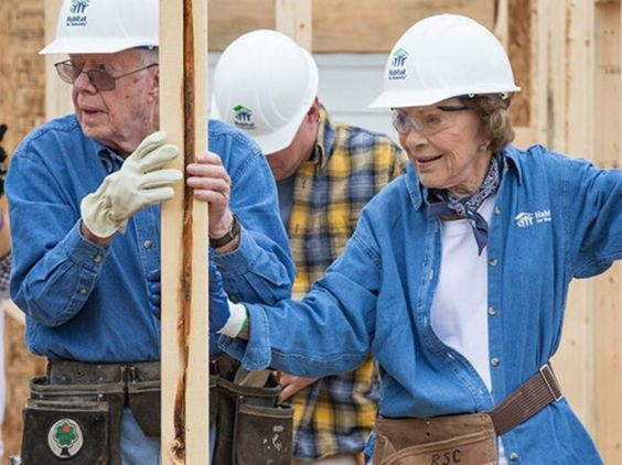 Jimmy and Rosalynn Carter wearing safety hats and tool belts on a construction site.