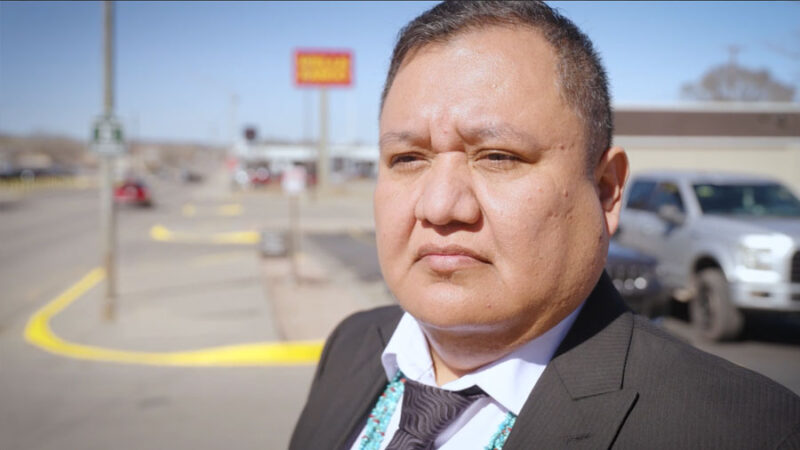 A man stands on a sidewalk and looks off camera