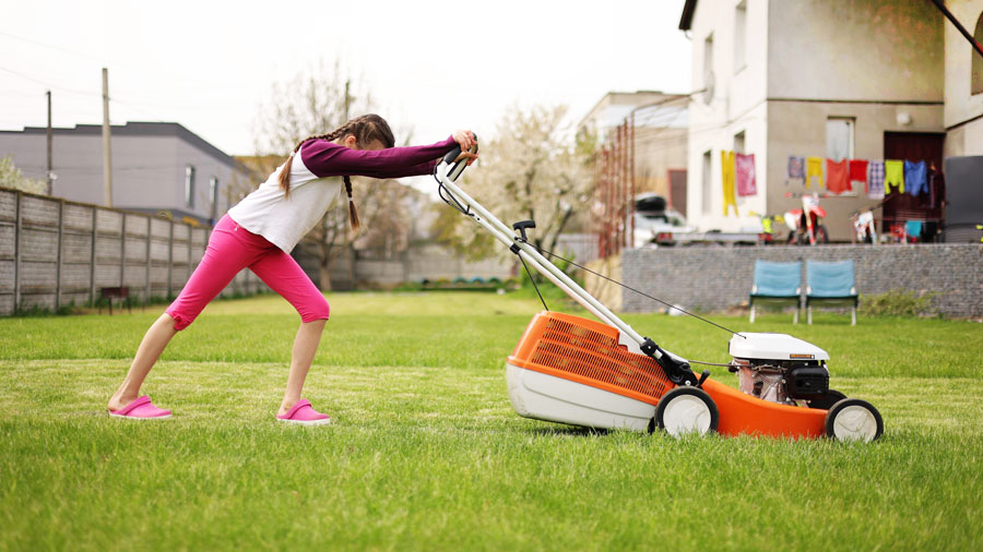 A teen pushes a lawn mower over a lawn of green grass.