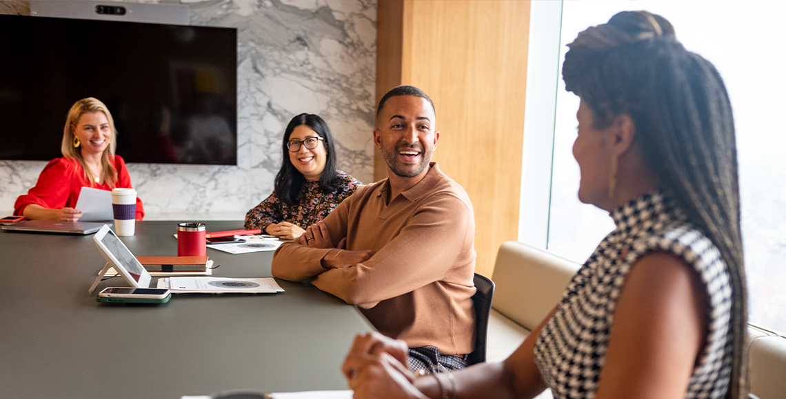 4 people are sitting at a conference table with smiles on their faces