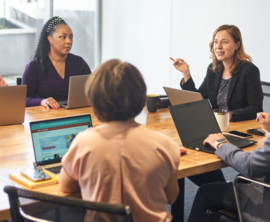 Five people sit around a conference table, each with a laptop in front of them.
