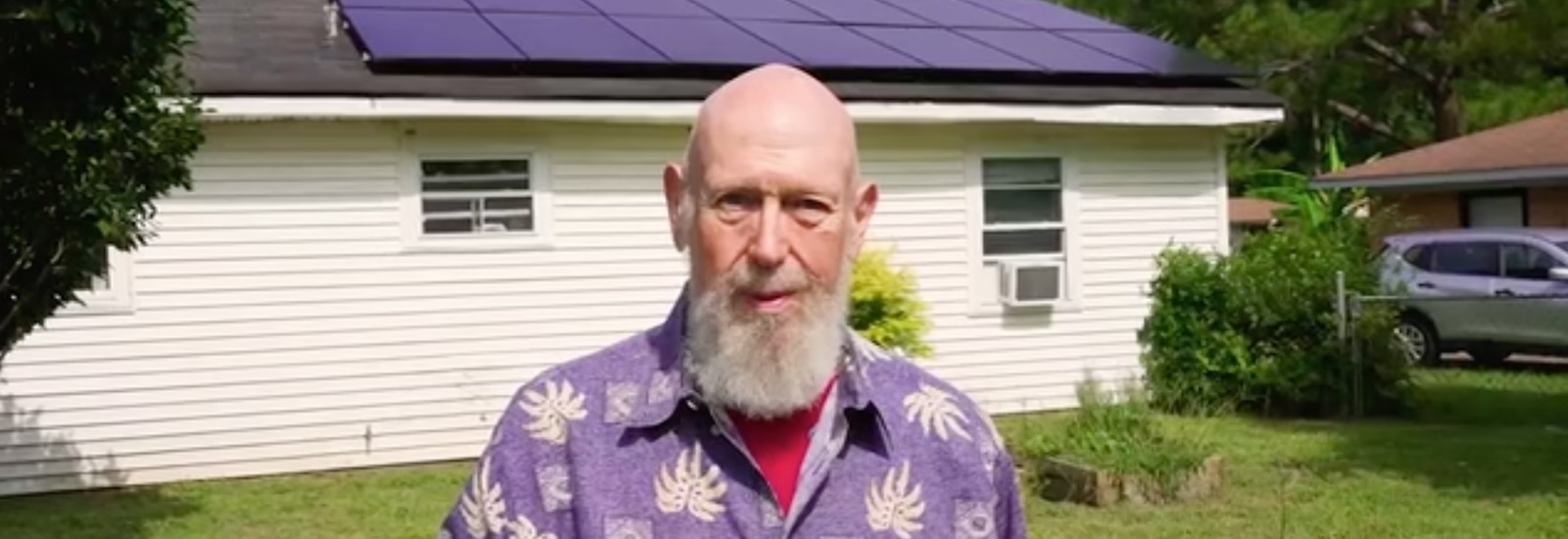 Marc Thomas stands in front of his house which has solar panels on the roof.