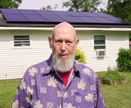 Marc Thomas stands in front of his house which has solar panels on the roof.