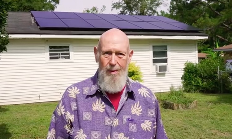 Marc Thomas stands in front of his house which has solar panels on the roof.