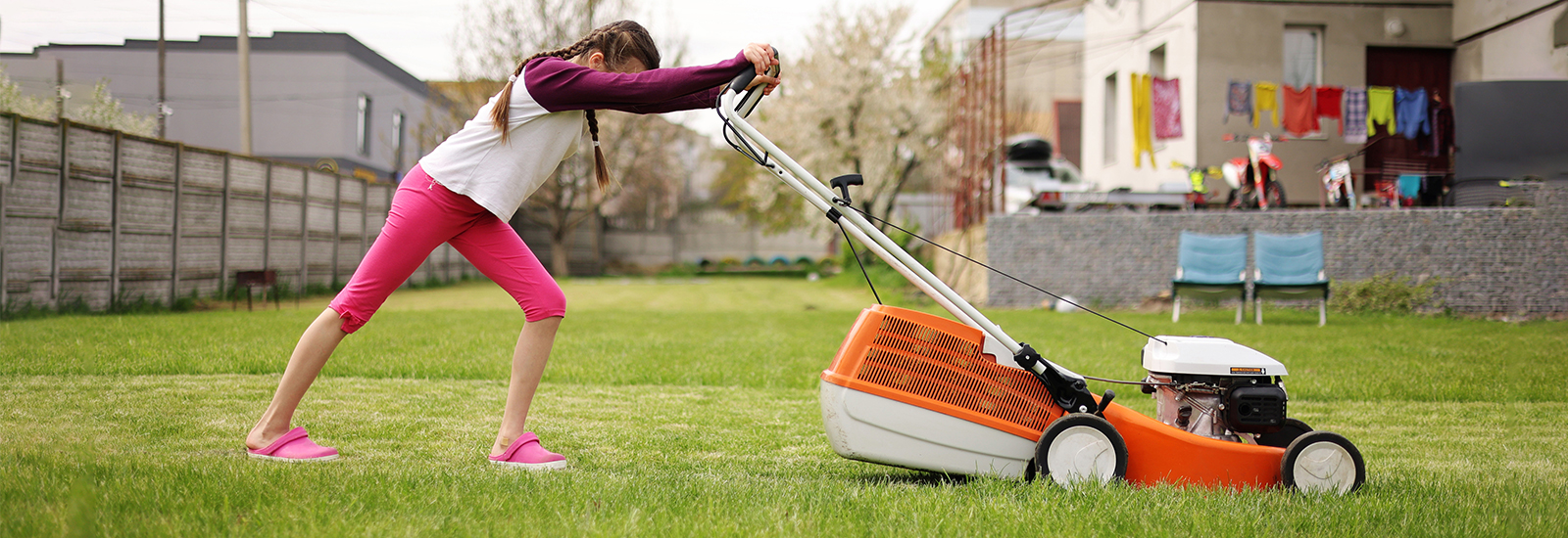 A teen pushes a lawn mower over a lawn of green grass.