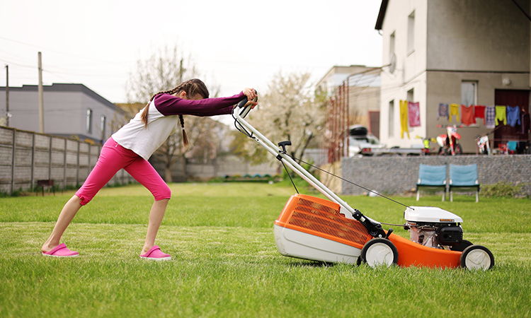 A teen pushes a lawn mower over a lawn of green grass.