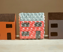 Three wooden toy houses in a row with the middle one wrapped in protective bubble wrap.