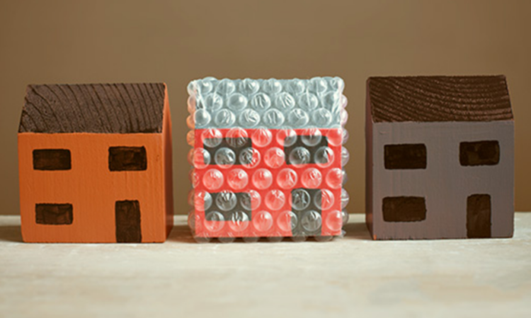 Three wooden toy houses in a row with the middle one wrapped in protective bubble wrap.