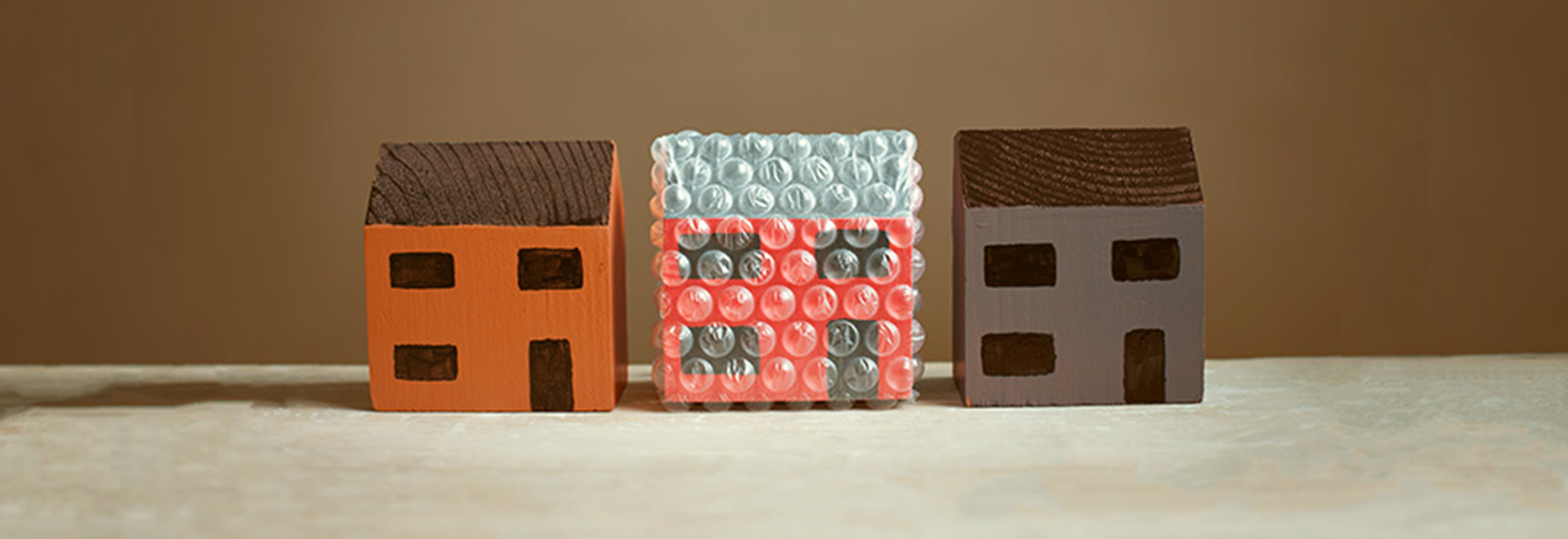 Three wooden toy houses in a row with the middle one wrapped in protective bubble wrap.