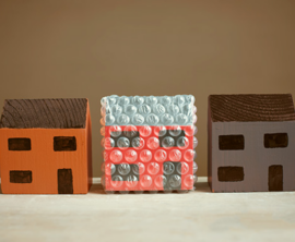 Three wooden toy houses in a row with the middle one wrapped in protective bubble wrap.