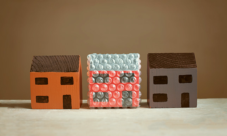 Three wooden toy houses in a row with the middle one wrapped in protective bubble wrap.